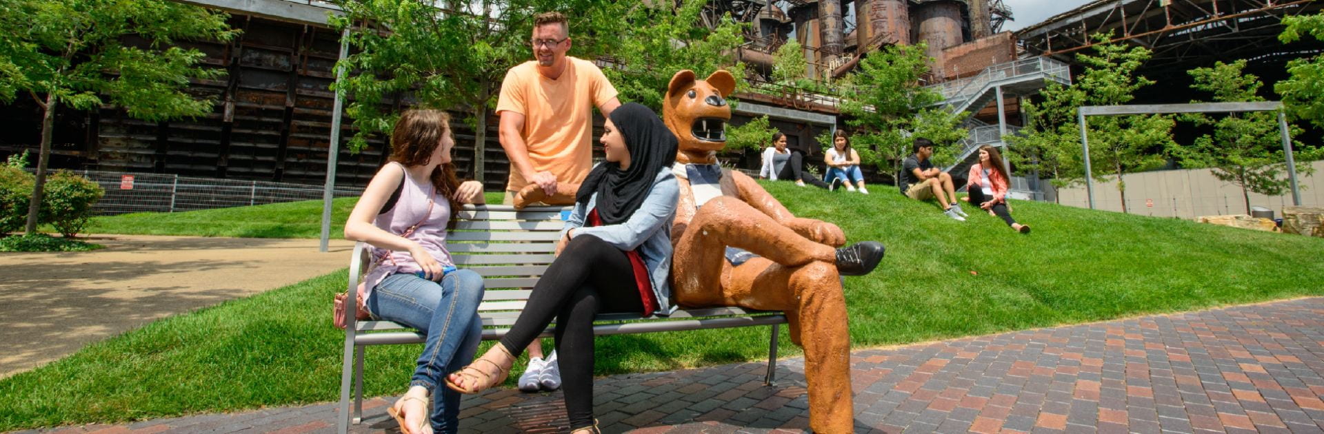 Three students sitting next to a Nittany Lion statue on a bench