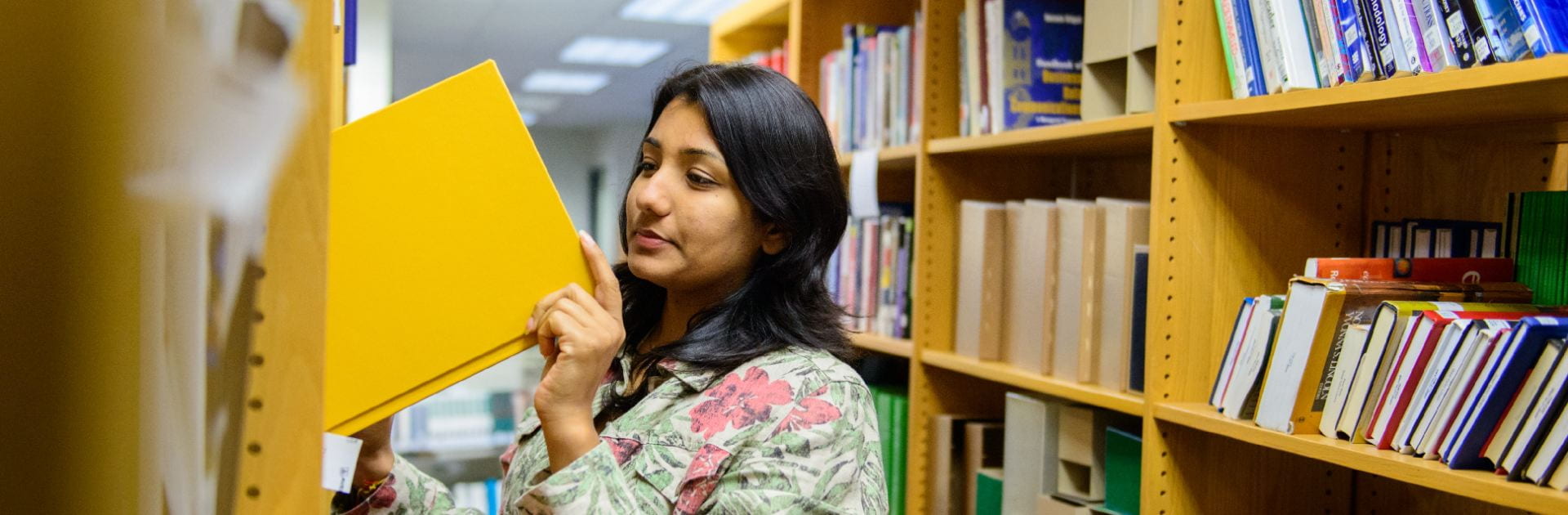 A woman removing a yellow book from a library bookshelf